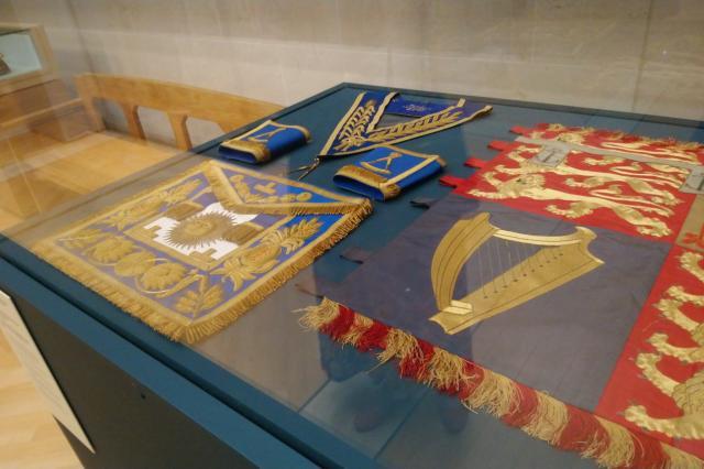 Embroidered banners and regalia laid out in a glass case