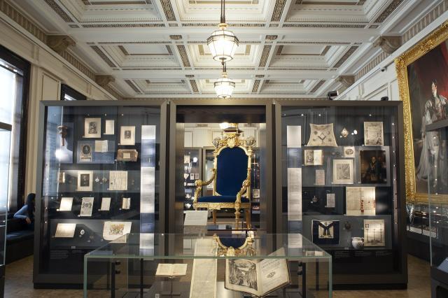 View of North Gallery showing large gold throne with blue cushions surrounded by glass display cases
